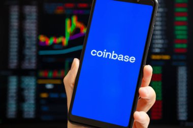 Ukraine, Odessa - October, 9 2021: Hand holding mobile with Coinbase app running at smartphone screen with trading page at background. Coinbase is American cryptocurrency exchange and trading platform