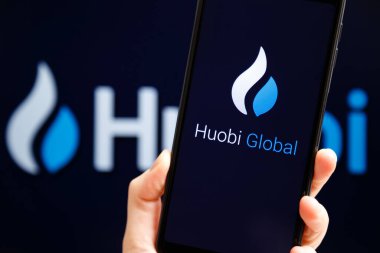 Ukraine, Odessa - October, 9 2021: Hand holding mobile with Huobi Global app running at smartphone screen with Huobi logo at background. Huobi is cryptocurrency exchange and trading platform