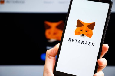 Ukraine, Odessa - October, 9 2021: Hand holding mobile with MetaMask app running at smartphone screen with metamask.io website at background. MetaMask is software crypto wallet