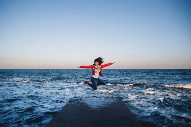 Sırt çantalı genç mutlu kız gün batımında sahile atlıyor.