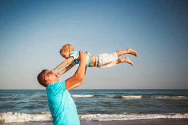 Happy father and son playing together at beach. Father throwing his son in the air