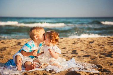 Small kids are kissing and having fun at beach together near the ocean, happy lifestyle family concept.