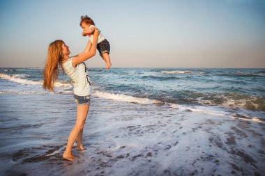 Happy mother and small daughter playing together at beach. Mom is throwing her kid in the air.