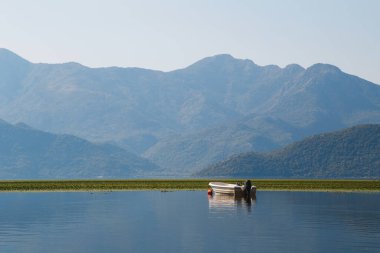 A beautiful view at a lonely boat in the middle of the lake Skadar with blue mountain view at background in Montenegro National Park, famous tourist attraction