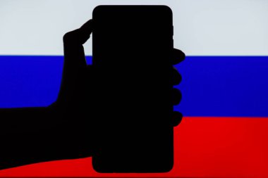 Silhouette of black hand holding mobile with Russian flag in background. Sanctions against Russia concept.