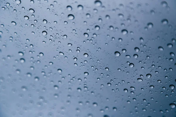 stock image Close up of rain drops on the windshield, front window of a car on a blue gray background of dark sky