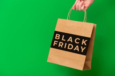 Black Friday, female hand holding brown craft shopping bag isolated on green background. Black friday sale, discount, shopping concept