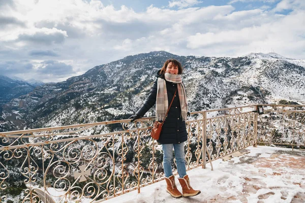 Vouraikos geçidinde dağın tepesindeki gözlem güvertesinde duran genç bir kadın. Karla kaplı muhteşem dağ manzaralı Mega Spileon Manastırı terası. Kış tatili Yunanistan