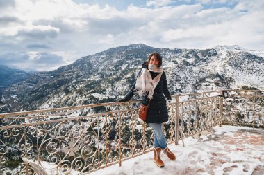 Vouraikos geçidinde dağın tepesindeki gözlem güvertesinde duran genç bir kadın. Karla kaplı muhteşem dağ manzaralı Mega Spileon Manastırı terası. Kış tatili Yunanistan