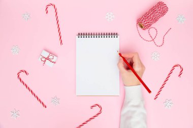 Noel arkaplanı. Kadın el yazısı boş deftere, şenlikli süslemeler, pastel pembeye hediye kutuları. Yeni yıl planlama, hedefler, yapılacaklar listesi veya dilek listesi konsepti. Düz yat, boşluğu kopyala