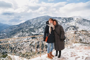 Vouraikos Vadisi 'ndeki Mega Spileon Manastırı' nın arka planında muhteşem kar manzaralı anne ve kız kucaklaşmasının kış portresi. Kış tatili Yunanistan