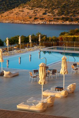 Güzel deniz manzaralı tatil köyünde boş iskemleli, masalı ve şemsiyeli lüks sabah yüzme havuzu. Yunan adası