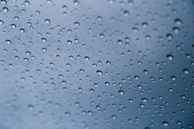 Koyu gökyüzünün mavi gri arkaplanına sahip penceredeki yağmur damlalarını kapat.