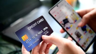 Elleri kredi kartı tutuyor ve online alışveriş için akıllı telefon kullanıyor.