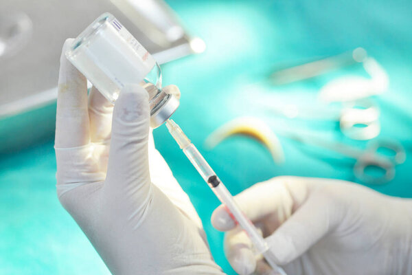 Hand holding syringe and medicine vial prepare for injection with surgical equipment and medicine vial background.