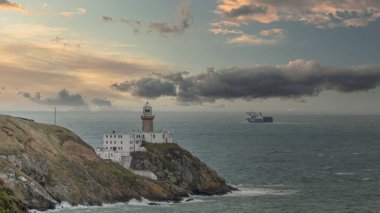 Baily Deniz feneri ve feribot ufukta, Howth Head Yarımadası güneşli ve bulutlu bir günde, deniz kıyısı, kayalar, manzara, Dublin, İrlanda, 12 Ekim 2021