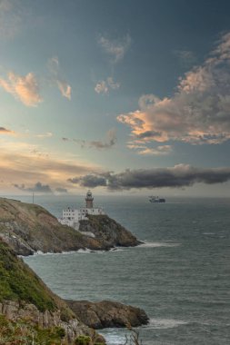 Baily Deniz feneri ve feribot ufukta, Howth Head Yarımadası güneşli ve bulutlu bir günde, deniz kıyısı, kayalar, manzara, Dublin, İrlanda, 12 Ekim 2021