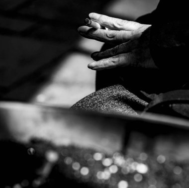 The hand of an elderly woman holding cigarette between her fingers, sitting beside a flower pot full of cigarette butts - stock photography.