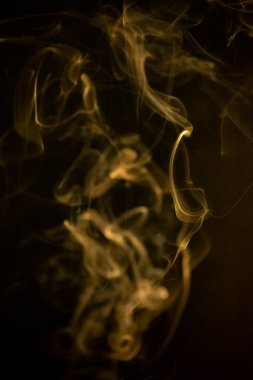 Sarı altın kıvrımlı, yükselen bir duman deseni siyah arka planda, fotoğraf arka plan, duman dokusu, soyut veya genel stok fotoğrafçılığı olarak kullanılabilir..