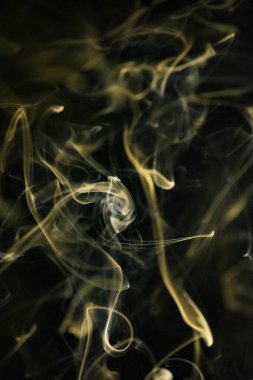 Siyah arka planda sarımsı altın rengi olan kıvrımlı, yükselen bir duman deseni, arka plan, duman dokusu veya soyut veya genel stok fotoğrafçılığı olarak kullanılabilir..