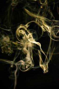 Siyah arka planda sarımsı altın rengi olan kıvrımlı, yükselen bir duman deseni, arka plan, duman dokusu veya soyut veya genel stok fotoğrafçılığı olarak kullanılabilir..