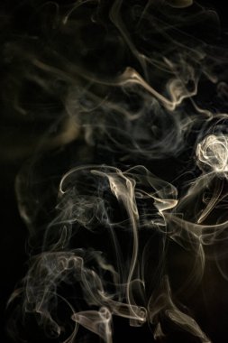 Siyah arka planda sarımsı altın rengi olan kıvrımlı, yükselen bir duman deseni, arka plan, duman dokusu veya soyut veya genel stok fotoğrafçılığı olarak kullanılabilir..