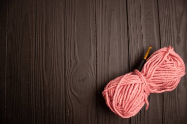 Koyu ahşap arka planda pembe iplik ve örgü kancası.