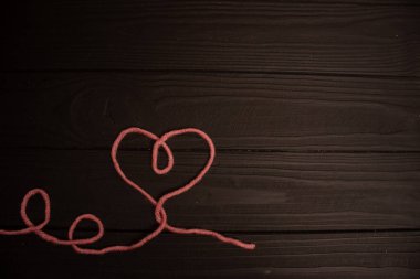 Koyu bir arkaplanda örgü örmek için pembe ipliklerin kalbi.