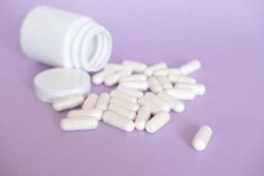 Mor arkaplandaki beyaz hapları ve kapsülleri fotokopi alanlarıyla kapatın. Ön plana odaklan, yumuşak bokeh. Eczane konsepti.