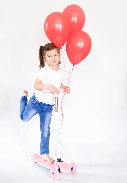 A four-year-old girl wears a sporty style and holds a childrens scooter. Photographed on a white background — Stock Photo, Image