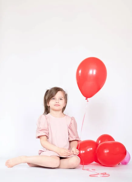 Cute little girl holding a bunch of red heart-shaped balloons — Stock Photo, Image