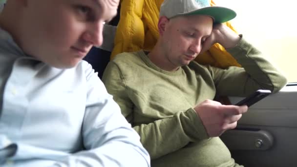 Deux hommes sont assis dans le train. Homme ennuyeux avec un téléphone tout en voyageant. — Video