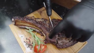 Eldivenli garson sulu bir biftek kesti. Restoran şefi az pişmiş biftek dilimliyor. Tahta üzerinde büyük bir bıçakla balta bifteği kesme işlemi. Sulu et eşit parçalara ayrılır..