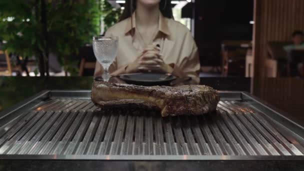 A fazer um bife de tomahawk. Carne suculenta rara a arder. Chef em luvas pretas prepara um requintado pedaço de carne grelhada na frente de um cliente em um restaurante. Pessoas irreconhecíveis. — Vídeo de Stock