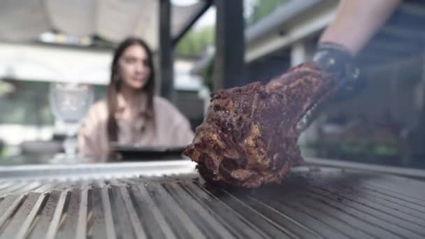 Stor tomahawkbiff. En kock i svarta handskar tillagar en utsökt bit grillat kött framför en kund på en restaurang. Sällsynt saftigt nötkött. Oigenkända människor. — Stockvideo