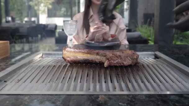 Transformar um bife gigante de tomahawk. Um chef de luvas pretas prepara um requintado pedaço de carne grelhada na frente de um cliente em um restaurante. Carne suculenta rara. Pessoas irreconhecíveis. — Vídeo de Stock