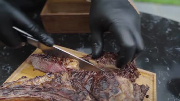 O garçom de luvas corta um bife suculento. Restaurante chef cortando bife de carne rara médio. Processo de corte de bife tomahawk com uma grande faca na placa de madeira. Carne suculenta é separada em pedaços pares. — Vídeo de Stock