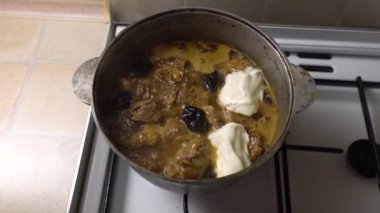 Sobanın üstünde eski bir kazanda yemek pişirirken sos ekliyorum. Erikli et pişirmenin geleneksel tarifi. Kaşıklı bir erkek eli. Ev yemeği..