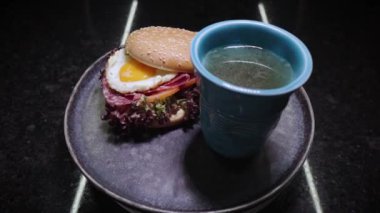Kızarmış yumurta ve bir bardak tavuk suyuyla sandviç. Dönüşümlü yemek. Sağlıklı beslenme. Mükemmel bir kahvaltı. Çok şık bir tabakla bir restoran yemeğinin sunumu. Bir aşçılık başyapıtı gösteriliyor.