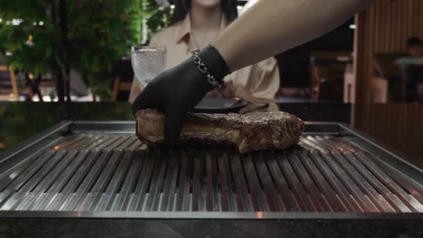 Mengubah steak tomahawk raksasa. Seorang koki dalam sarung tangan hitam menyiapkan sepotong daging panggang yang indah di depan pelanggan di sebuah restoran. Daging sapi yang langka. Orang yang tak dikenal. — Stok Video