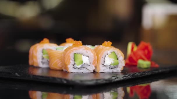Užívání sushi pomocí bambusových tyčinek v japonské restauraci. Lahodná Philadelphie se válí na černé kamenné desce. Sushi z lososa, rýže, kaviárový sýr. Vynikající jídlo. Tradiční asijské jídlo. — Stock video