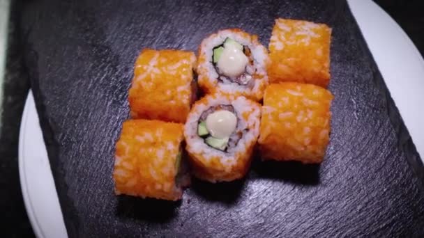 Vista superior de rolos de sushi frescos girando na placa de ardósia de pedra preta. Close-up tiro de sushi de peixe, salmão, arroz, abacate. Comida deliciosa. Tradicional comida asiática. — Vídeo de Stock