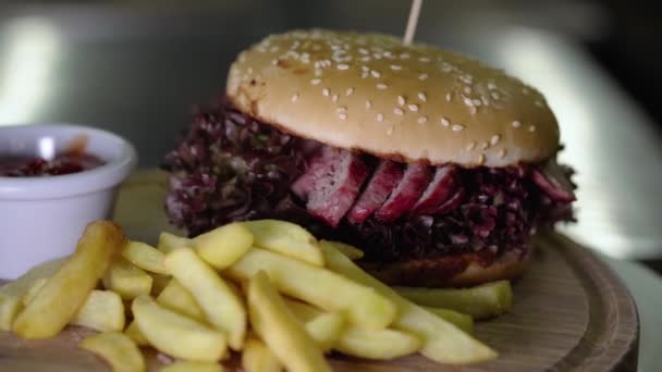 Konsep makanan cepat saji. Appetizing burger daging sapi berputar di meja kayu. Masakan closeup lezat. Hamburger dan kentang goreng perlahan-lahan berputar. — Stok Video