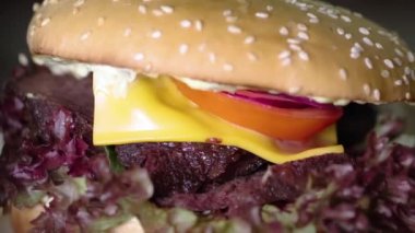 Ahşap masada dönen dilimlenmiş biftekli büyük bir burger. Fast Food Konsepti. Yemekler çok lezzetli. Biftek, salata, domates ve peynirli lezzetli hamburger yakın çekim.