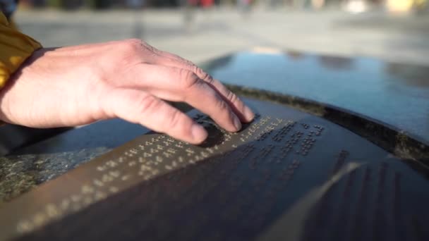 Az ember Braille betűtípussal írt szöveget olvas, napos nap utcai táblán. Szabadságon lévő személyek, a fogyatékkal élők turista leírása. — Stock videók