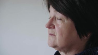 Yaşlı bir kadın bakışlarını kameraya ve sırtına çevirir. Yaşlı bir kadının yüzü ve gözleri. Annemin yüzünde büyük kırışıklıklar var. Yüzünü yaklaştır. Yaşlı bir vatandaş kameraya bakar..