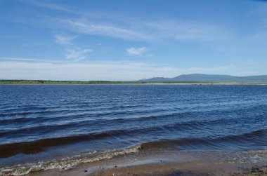 Nehir kıyısında dalgalar. Açık gökyüzü ve zıt kıyıların görüntüsü.