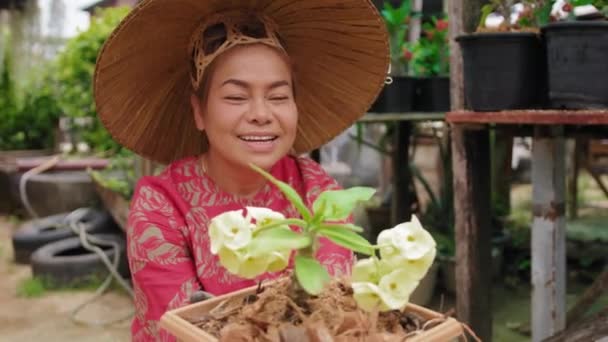 Mujer asiática con sombrero de paja vietnamita sonriendo, sosteniendo flor en maceta en el jardín — Vídeos de Stock