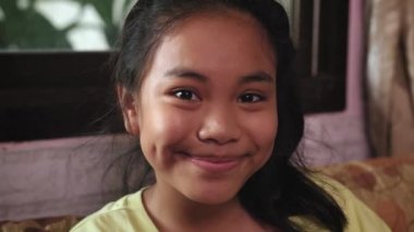 Genç Asyalı kız evdeki kanepede otururken kameraya bakıyor.