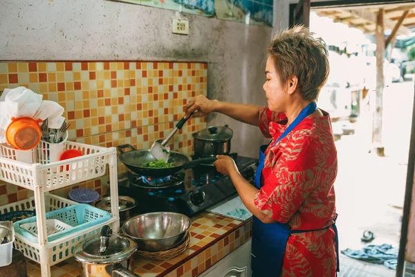 Asian woman short hair in red dress cooking stir fried vegetables in kitchen — Stock Photo, Image